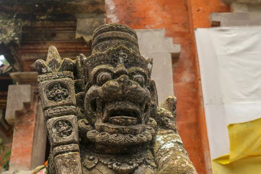 A close up on a guardian figure next to a Hindu temple on Bali, Indonesia. A bricked entrance gate to a Hindu temple on Bali. Traditional and historical site. Sculpture of a Balinese temple guardian.