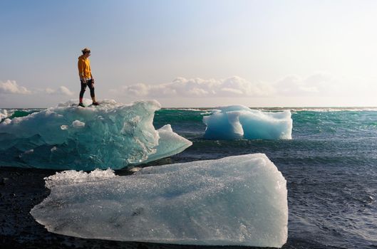 Tourist standing on an iceberg at the Diamond Beach in Jokulsarlon Glacier Lagoon in Iceland. This beach is known for its large ice rocks lying on the lava black sand.