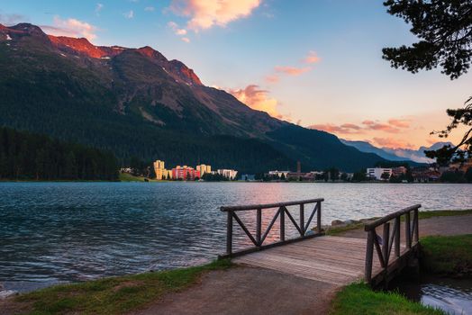 Sunset above St. Moritz with lake also called St. Moritzsee, a wooden footbridge in the foreground and Swiss Alps in the background in Engadin, Switzerland.