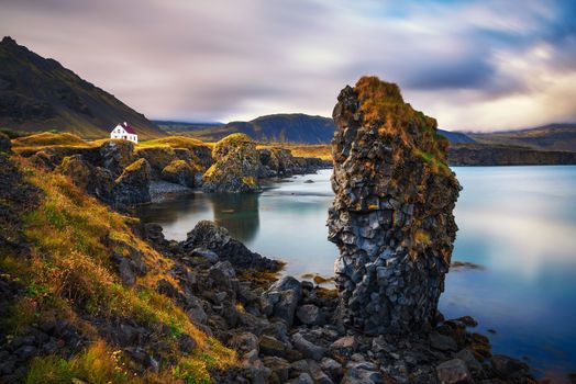 Atlantic sea shore of Snaefellsnes peninsula in Iceland with big cliffs and a small white house in the village of Arnarstapi. Long exposure.