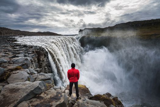 Young hiker standing close to the Dettifoss waterfall located on the Jokulsa a Fjollum river in Iceland. Dettifoss is the second most powerful waterfall in Europe after the Rhine Falls.