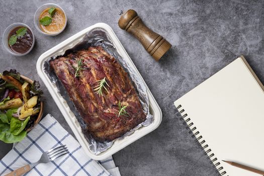 Closeup of pork ribs grilled with BBQ sauce and caramelized in honey with Vegetables and sauces on a drak table, prepared food.