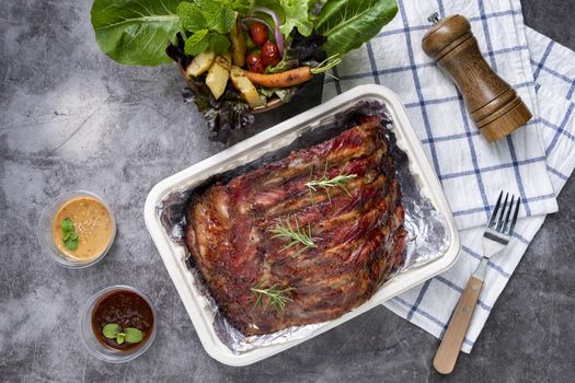 Closeup of pork ribs grilled with BBQ sauce and caramelized in honey with Vegetables and sauces on a drak table, prepared food.