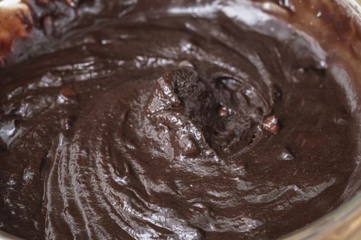 Melted chocolate swirl background, Baker or chocolatier preparing chocolate bonbons whisking the melted chocolate with a whisk dripping below.