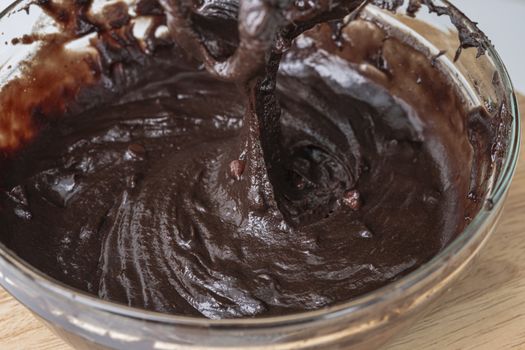 Melted chocolate swirl background, Baker or chocolatier preparing chocolate bonbons whisking the melted chocolate with a whisk dripping below.
