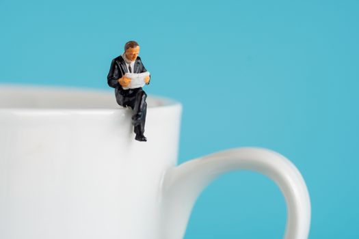 business miniature figures sitting and read a book, read newspaper, waiting, talking and relax on white cup of hot coffee.