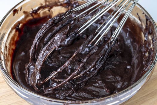 Melted chocolate swirl background, Baker or chocolatier preparing chocolate bonbons whisking the melted chocolate with a whisk dripping below.