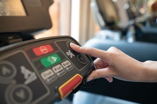 closeup of young woman athlete running on treadmill in gym. push on control panel