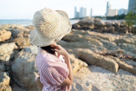 Back view of young woman sitting on the rock at the beach