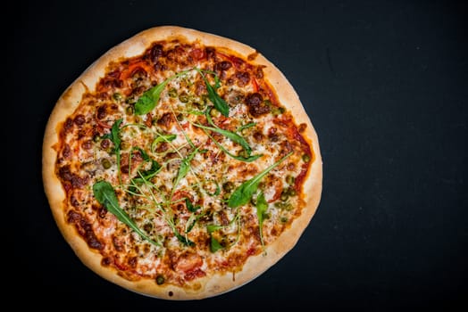 Italian pizza with greens on the black table with empty place