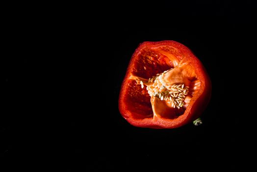 Fresh cut Bulgarian red pepper with seeds inside on a black background