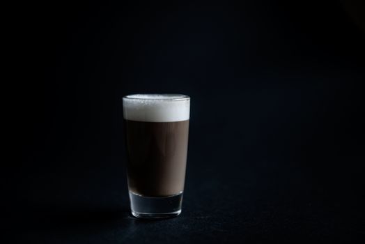 mini cup of cappuccino in a glass cup on black background with copyspace