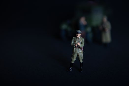 Toy a figure of a man in a military German uniform. In the background of a vague truck