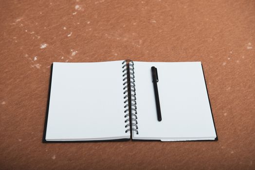 open spiral notebook to point with a pen on a brown background