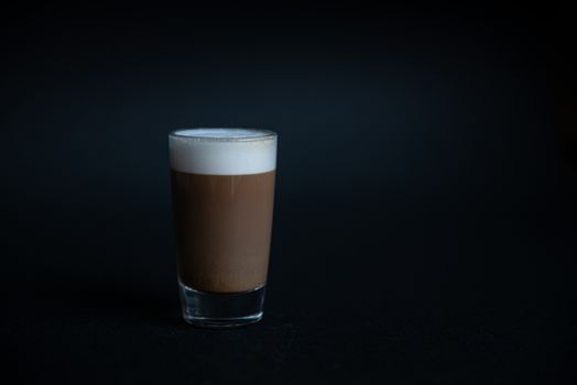 mini cup of cappuccino in a glass cup on black background with copyspace