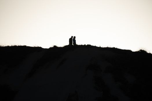 SIlhouette of a couple walking at sunset on a hill.