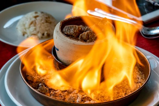 Traditional Turkish Testi Kebab cooked in clay pot over fire on the table.
