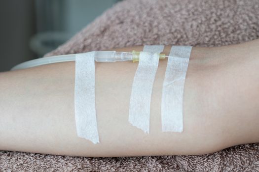 Patient with intravenous drip receiving saline solution. Injecting needle in to the arm.