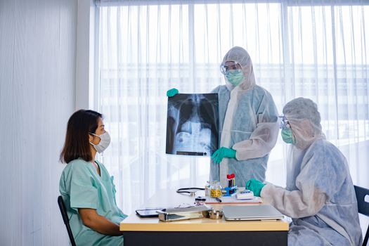 Asian doctor in personal protective equipment or ppe explain the x-ray film of covid-19 or coronavirus infection to patient in the hospital. coronavirus, covid-19 outbreak, or medical hospital concept