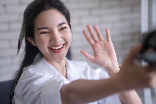 beautiful young asian woman smiling while selfie in front of camera against white brick wall