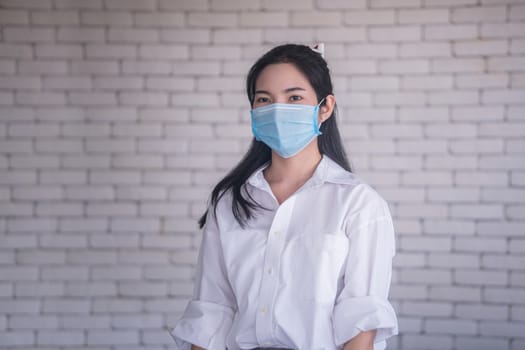 beautiful young asian woman wearing face mask to protect covid19 virus against white brick wall