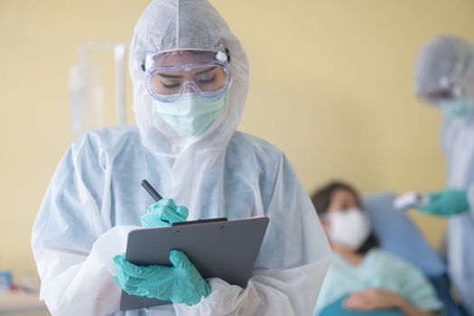 asian woman doctor in personal protective suit or PPE with mask writing on quarantine patient chart, for screening coronavirus. Coronavirus, covid-19 concept.