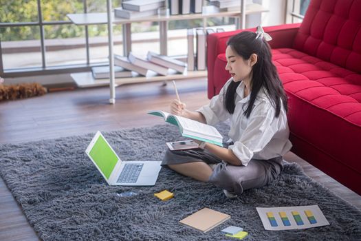 top view of young asian woman working with laptop computer in the living room. Work from home and study at home concept.