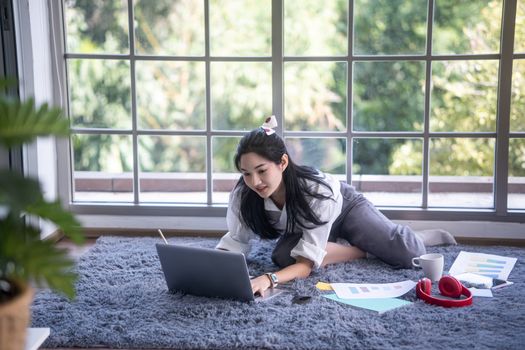 top view of young asian woman working with laptop computer in the living room. Work from home and study at home concept.