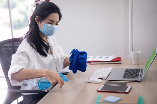 young asian woman cleaning her computer desk and equipment to protect covid19 virus infection