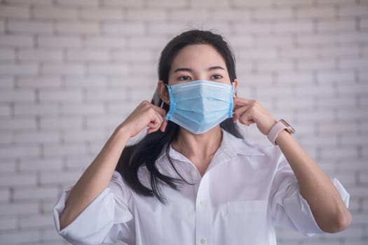 beautiful young asian woman wearing face mask to protect covid19 virus against white brick wall