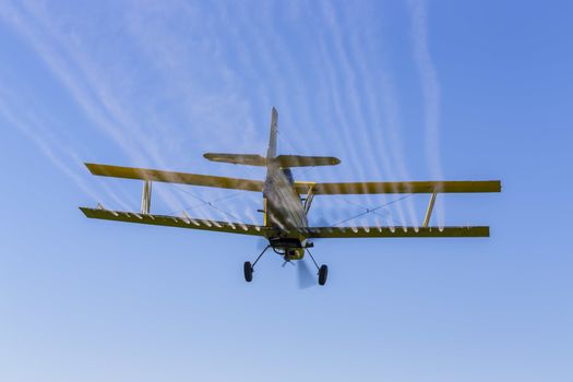 A crop duster applies chemicals to a field of vegetation.