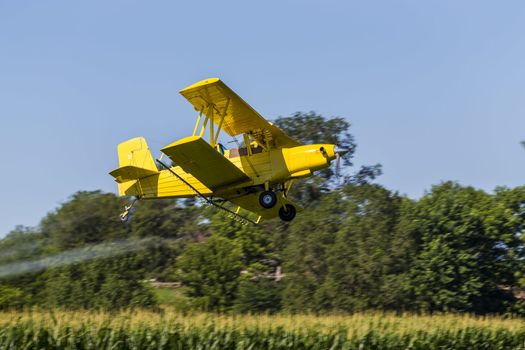 A crop duster applies chemicals to a field of vegetation.