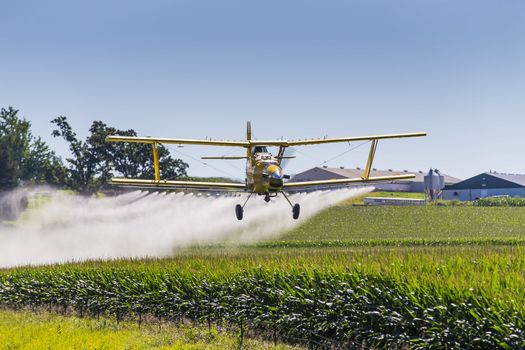 A crop duster applies chemicals to a field of vegetation.
