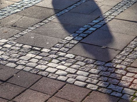 Shadows of people in a shopping area on a cobblestone ground