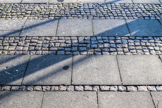 Shadows of people in a shopping area on a cobblestone ground