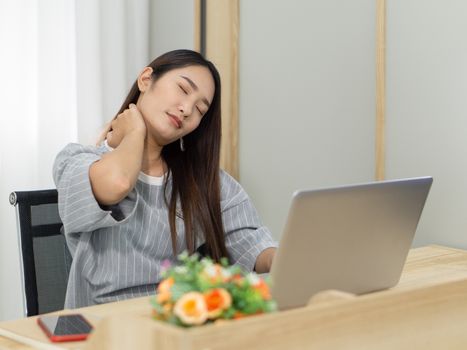 Young woman studying online at home using laptop computer. Use her hand to massage the neck to relieve fatigue.