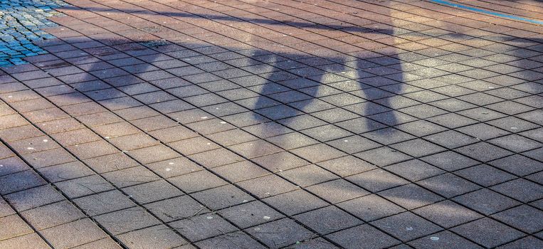 Shadows of people in a shopping area on a cobblestone ground