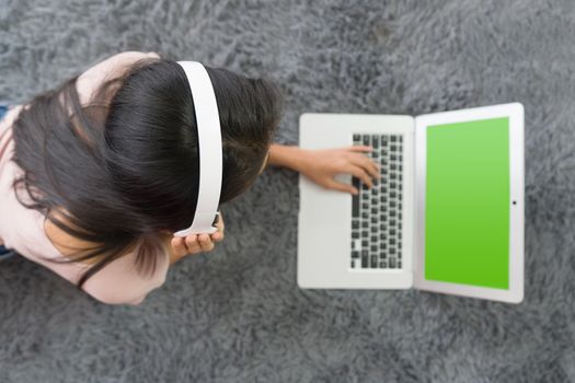 Teen wearing headphones using  laptop computer with green screen relax in living room, enjoy leisure weekend at home. Stress free concept. Top View