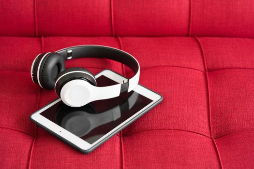 White modern headphones and tablet computer on red sofa. Online music concept