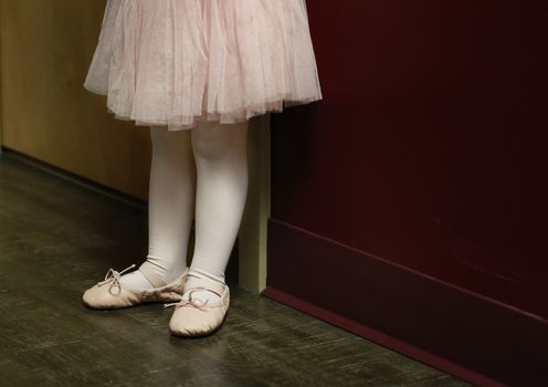 Classical ballet school: legs of little ballerina in ballet shoes at the wall