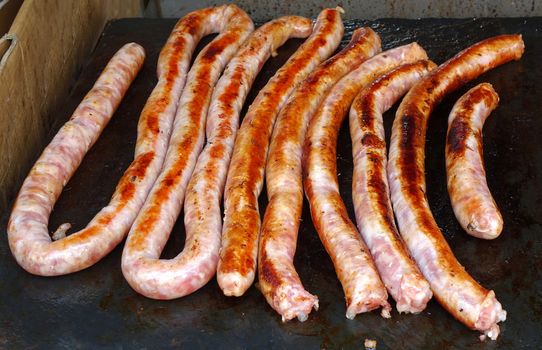 An outdoor vendor roasts fresh pork sausages on a grill