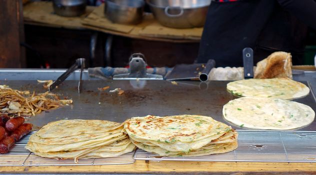 A street food stall offers pancakes with spring onions cooked on a hot griddle