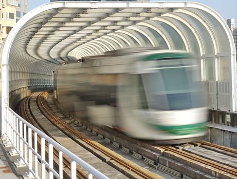 A light rail train emerges from a tunnel with transparent panels