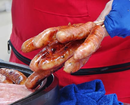 An outdoor vendor holds a bunch of ready-to-eat grilled sausages
