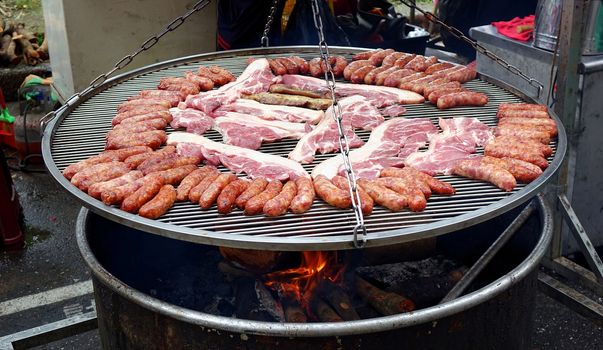 A street vendor cooks sausages and slabs of pork on a large barbecue rack