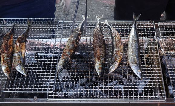 A street vendor cooks Pacific saury on a charcoal grill

