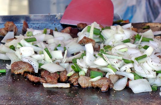 An outdoor vedor cooks meat, onions and leeks on a Teppanyaki griddle