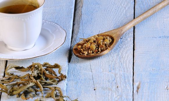 Cup of chamomile and herbs on wooden table in the kitchen.