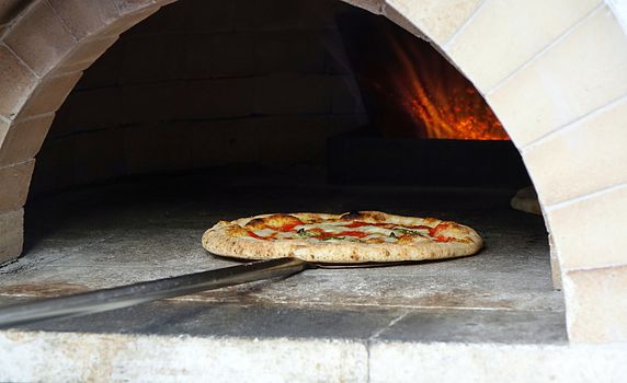 Pizza margherita with tomatoes, cheese and fresh basil is baking in the oven