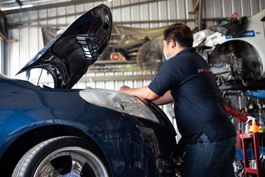 Bangkok, Thailand - April 4, 2020 : Unidentified car mechanic or serviceman checking a car engine for fix and repair problem at car garage or repair shop